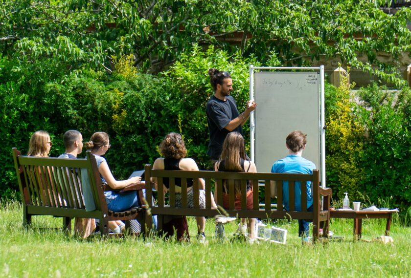 Tutor writing on whiteboard in college garden with other students watching