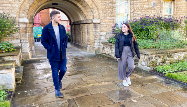 Two students walking and talking through college archway
