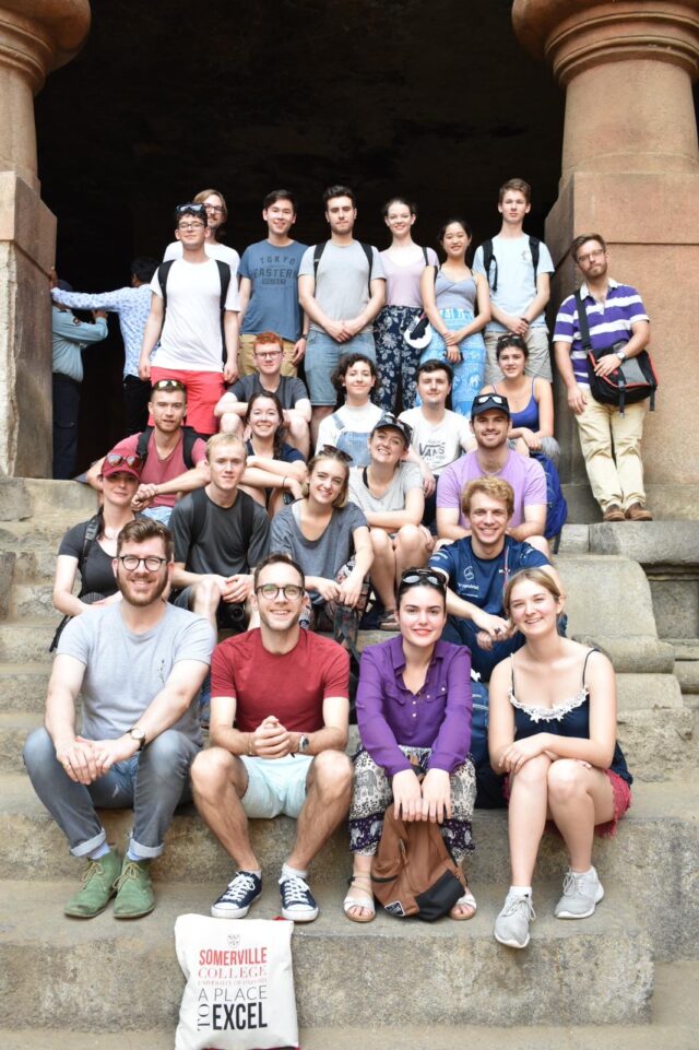 Somerville College Choir members sitting on stone steps between two large columns