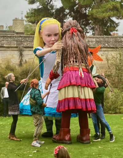 The Story Museum's Alice in Wonderland Puppet embraces Little Amal. Both puppets are 3.5m tall. 