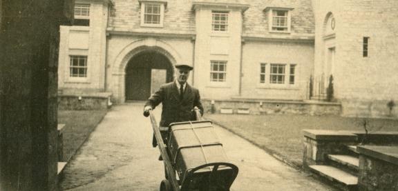 Old sepia image of a porter pushing a trunk through Darbishire Quad
