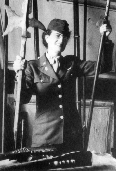 A woman in army uniform holds up an ancient looking axe