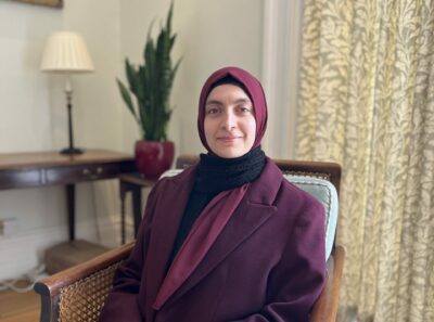 A young woman wearinga purple jacket and hijab smiles at the camera