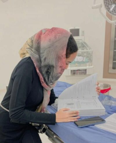 A young woman wearing a hijab consults a huge textbook.