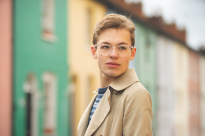 A white young man looks pensively in a street with brightly coloured houses