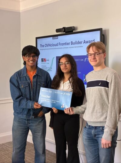 Three students smile at the camera, holding a voucher they have just received
