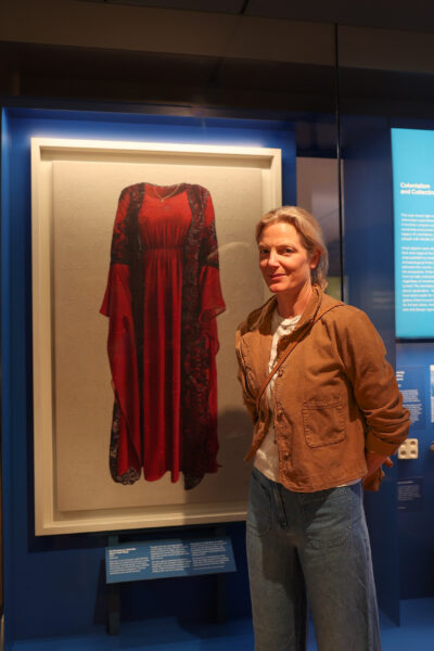 A woman stands in front of a hanging paitning of a red dress