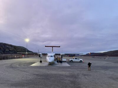 A small plane sits in a sparse landscape, with a very large pale sky above.
