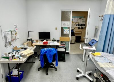 A clinical room with a desk, chair, and various medicial equipment.