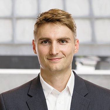 A man in a shirt and jacket smiles at the camera