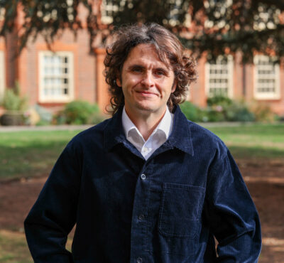 A man smiles at the camera wearing a dark blue courderoy jacket
